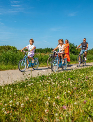 Una familia monta en bicicleta por un sendero cerca de un parque vacacional con alojamiento glamping.