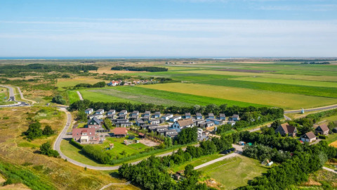 Vista aérea de un parque vacacional con alojamientos glamping, rodeado de campos verdes y naturaleza.