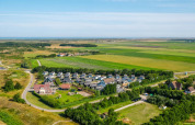Luftfoto af et feriepark med glamping-indkvartering, omgivet af grønne marker og åbent landskab.