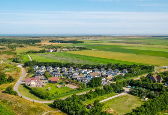 Luchtfoto van een vakantiepark met glamping verblijven, middenin het groen en uitgestrekte weilanden.