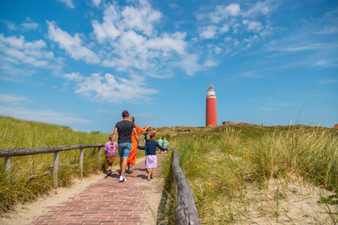 Gezin wandelt op een pad naar een vuurtoren in een vakantiepark met glampingverblijven.