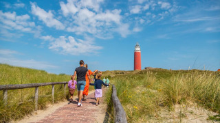 Familie spaziert auf einem Pfad durch Dünen nahe einem Leuchtturm in einem Glamping-Ferienpark.