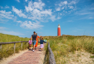 Family walking along a sandy path towards a lighthouse at a holiday park offering glamping accommodations.