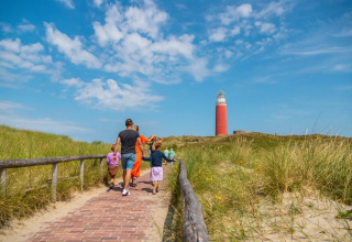 Gezin wandelt op een pad naar een vuurtoren in een vakantiepark met glampingverblijven.