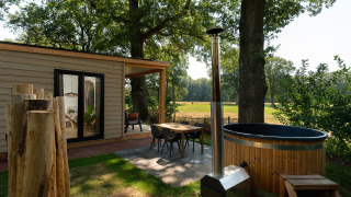 Outdoor area of a tiny house with wooden facade, sauna, and hot tub at Holiday Park Mölke, Netherlands.