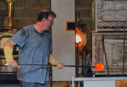 Mann bei der Glasbläserei in einer Werkstatt bei Quimper, Bretagne, Frankreich, mit Ofen sichtbar.