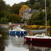 Boote auf einem ruhigen Gewässer, ein Haus und herbstliche Bäume nahe Quimper in der Bretagne, Frankreich.