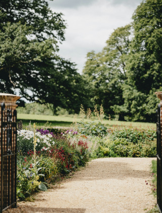 Offenes Gartentor mit Kiesweg, umgeben von bunten Blumen und Bäumen nahe Quimper in der Bretagne.