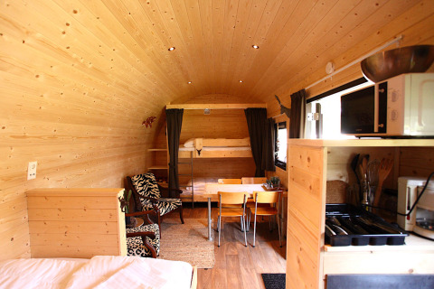 Cozy glamping accommodation with wooden interior, dining area, kitchenette, and comfy lounge chair.