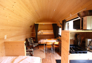 Alojamiento de glamping acogedor con interior de madera, comedor, cocina y zona de descanso.