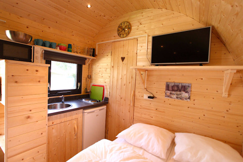 Cozy glamping cabin interior with wood walls, kitchenette, double bed, wall-mounted TV and decorations.