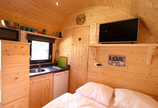 Acogedora cabaña de glamping con paredes de madera, cocina pequeña, cama doble y televisor de pared.