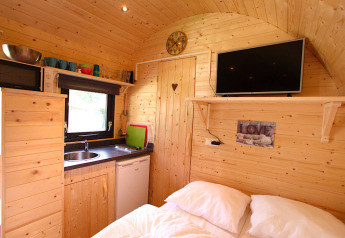 Acogedora cabaña de glamping con paredes de madera, cocina pequeña, cama doble y televisor de pared.