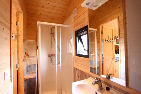 Bagno moderno in un alloggio glamping con pareti in legno, cabina doccia, lavandino e finestra.
