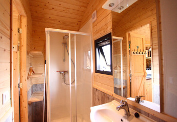Bagno moderno in un alloggio glamping con pareti in legno, cabina doccia, lavandino e finestra.