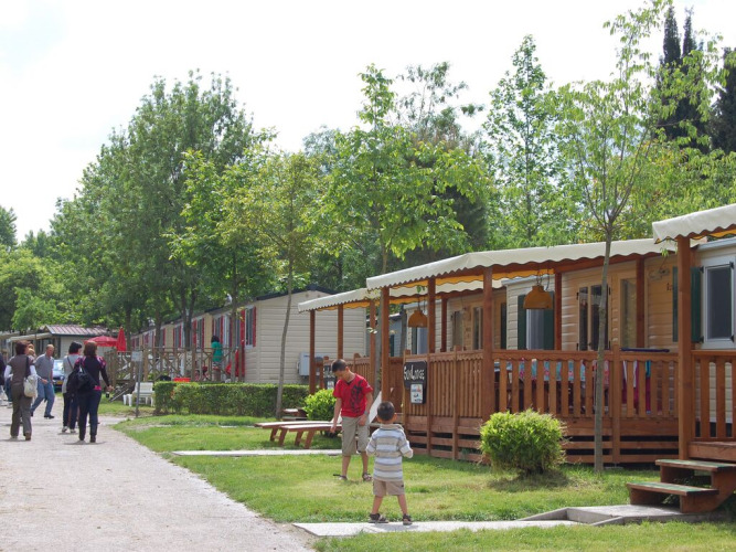 Personas pasean y niños juegan frente a cabañas de madera en un entorno verde y tranquilo de una posada.