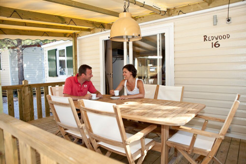 Dos personas toman café en la terraza de SunLodge Redwood 16, sentados en una mesa de madera al aire libre.