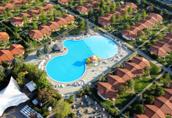 Vue aérienne d’un lodge avec des bungalows aux toits rouges et une grande piscine au centre verdoyant.