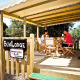 Two people have breakfast on the wooden SunLodge porch, surrounded by trees at a peaceful campsite.