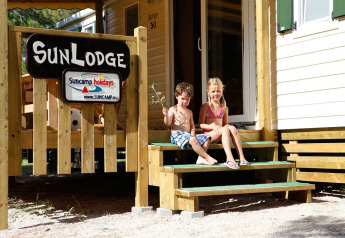 Due bambini seduti sui gradini davanti a una SunLodge con veranda in legno in una giornata soleggiata.