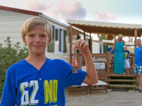 Niño con camiseta azul sostiene una llave frente a SunLodge Redwood, familia está detrás fuera de la cabaña.