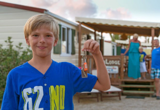 Ragazzo con maglietta blu tiene una chiave davanti a SunLodge Redwood, famiglia sullo sfondo fuori dal lodge.