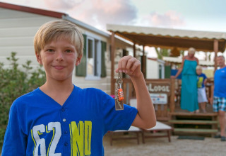 Niño con camiseta azul sostiene una llave frente a SunLodge Redwood, familia está detrás fuera de la cabaña.