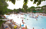 Piscina exterior en un lodge con niños y adultos jugando en el agua, rodeados de tumbonas y árboles verdes.