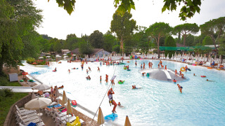Piscina exterior en un lodge con niños y adultos jugando en el agua, rodeados de tumbonas y árboles verdes.