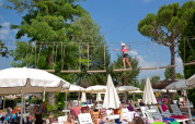 Barn balancerer på forhindringsbane over solsenge og parasoller ved en udendørs swimmingpool i lodgen.