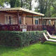 Solrige SunLodge Aspen-hytter og liggestole i Altomincio Family Park, Italien, omgivet af grønne træer.