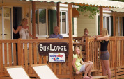 Vijf personen ontspannen op het terras van SunLodge Maple met houten hek en witte ligzetels.