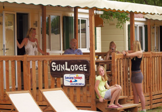 Cinque persone si rilassano sulla terrazza di SunLodge Maple con recinzione in legno e lettini bianchi.