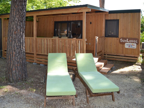 Two green loungers in front of SunLodge Catalpa at hu Norcenni Girasole Village, Italy, surrounded by trees.