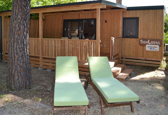 Two green loungers in front of SunLodge Catalpa at hu Norcenni Girasole Village, Italy, surrounded by trees.
