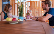 Una familia comparte una comida en una mesa de madera en la terraza de SunLodge Catalpa rodeada de madera.