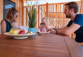 Una familia comparte una comida en una mesa de madera en la terraza de SunLodge Catalpa rodeada de madera.