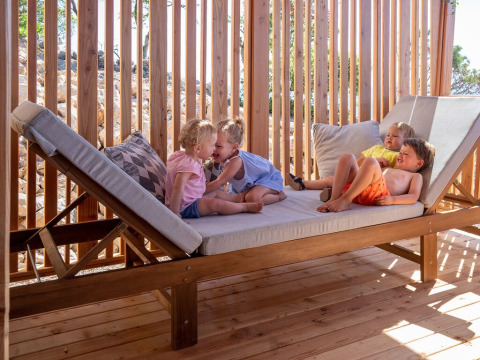 Vier jonge kinderen spelen en rusten op een groot houten ligbed bij SunLodge Catalpa in de zon.