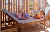 Vier jonge kinderen spelen en rusten op een groot houten ligbed bij SunLodge Catalpa in de zon.