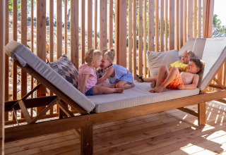Four young children play and relax on a large wooden daybed at SunLodge Catalpa, enjoying the sunshine.