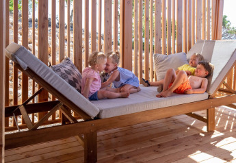 Vier jonge kinderen spelen en rusten op een groot houten ligbed bij SunLodge Catalpa in de zon.