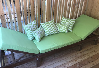 Groene ligstoel met kussens op houten terras bij SunLodge Catalpa, een wand van houten latten achteraan.