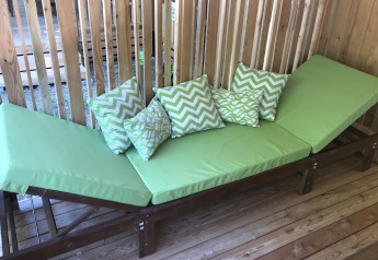 Groene ligstoel met kussens op houten terras bij SunLodge Catalpa, een wand van houten latten achteraan.