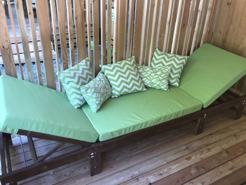 Groene ligstoel met sierkussens op houten terras bij SunLodge Catalpa, houten lattenwand op de achtergrond.