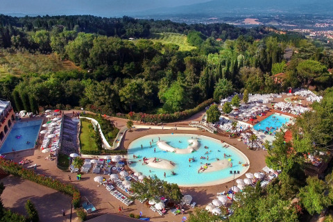 Luchtzicht op een lodge met verschillende zwembaden, ligstoelen en groene omgeving op een heuvelachtig terrein.