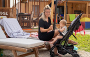 Vrouw met kindje in buggy geniet buiten bij SunLodge BigLeaf tegen houten lodge en terrasmeubilair.