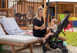 Donna con un bambino in passeggino si rilassa all'aperto presso SunLodge BigLeaf davanti a bungalow in legno.