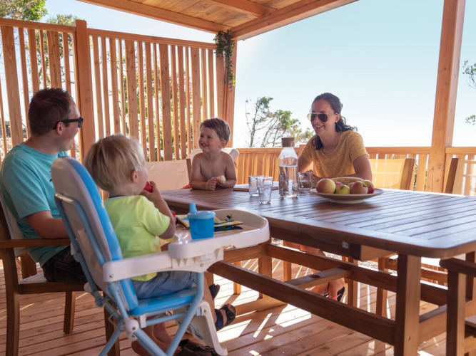 Una familia disfruta de una comida junta en la terraza de madera de SunLodge BigLeaf, rodeada de naturaleza.