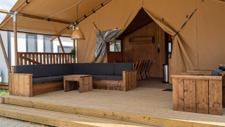 Spacious glamping tent with wooden deck, large sofa, and cozy seating area in a campsite setting.