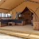 Udendørs loungeområde med træmøbler og teltdug, set ved en glampingbolig på en campingplads.